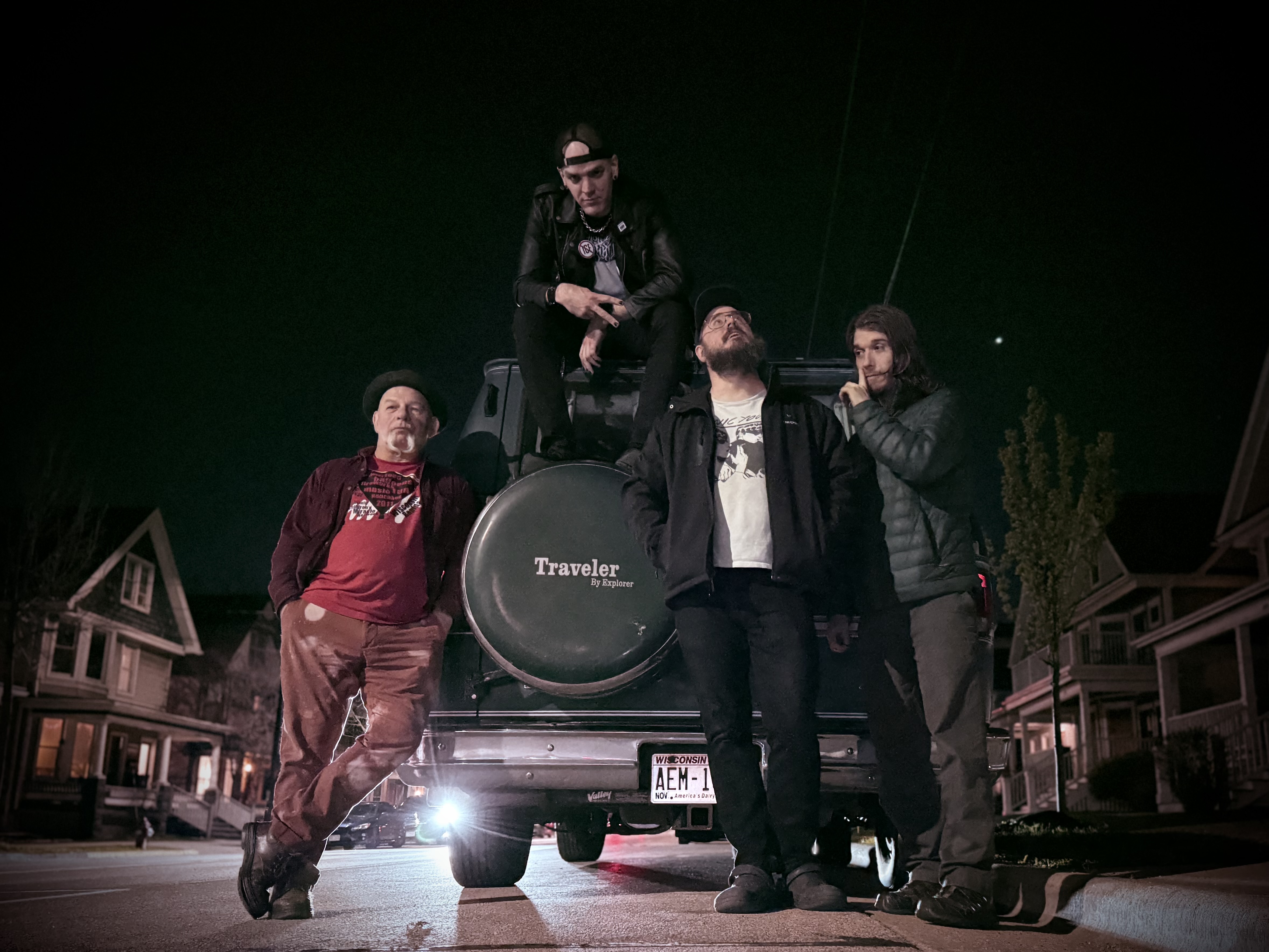 The four members of The Pistols at Dawn posing together at night in front of a vehicle on a Madison street