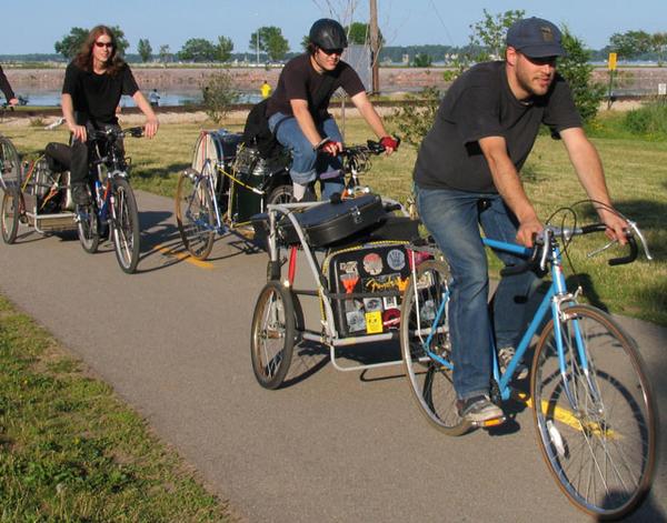 Early promotional image of The Pistols at Dawn riding bicycles with instruments and gear