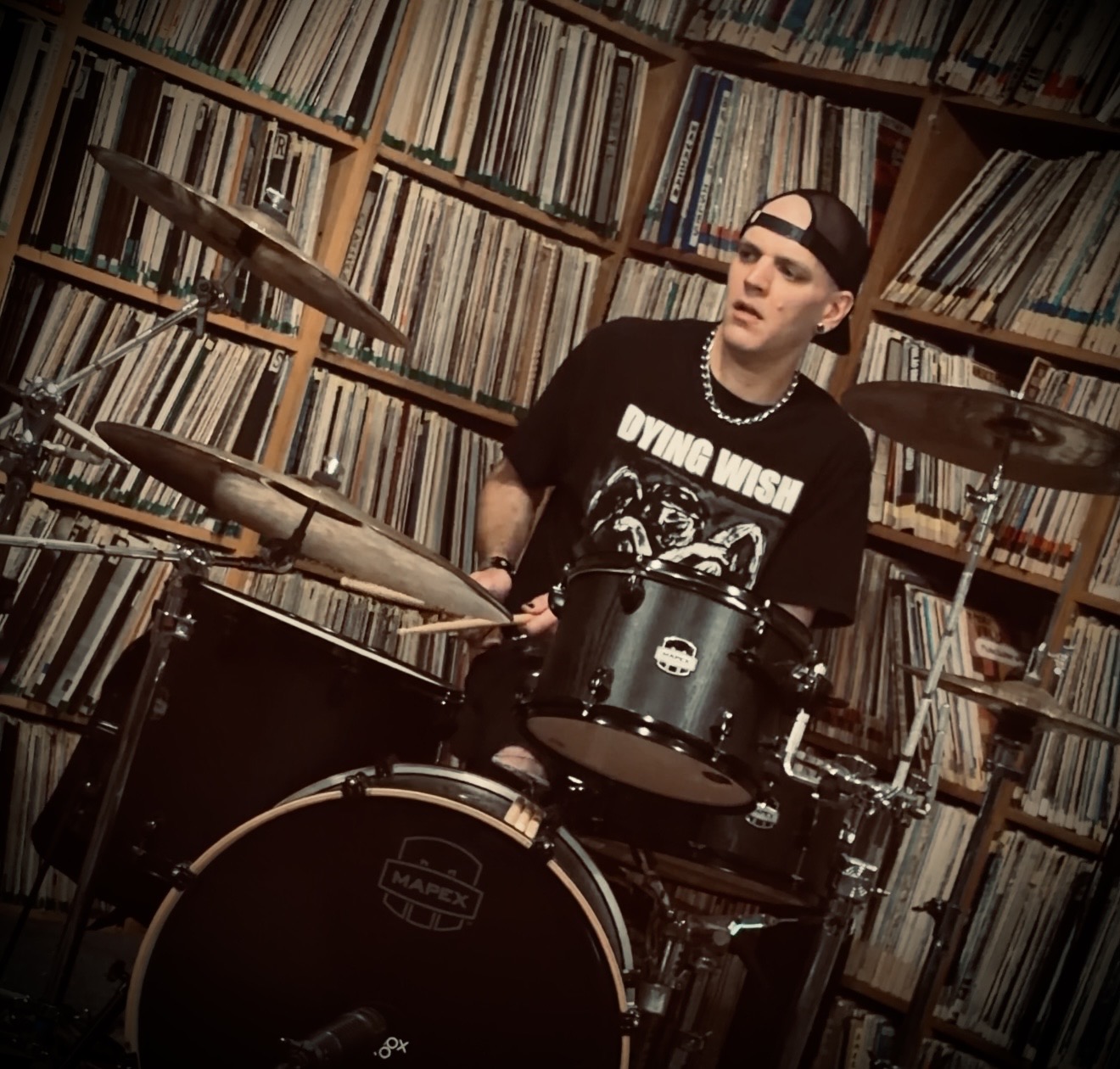 Alex playing a black Mapex drum kit in a room lined with records